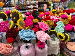 A vibrant selection of handcrafted flowers and roses made from multicolored yarn, beautifully arranged in a local market.