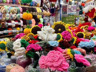 A vibrant selection of handcrafted flowers and roses made from multicolored yarn, beautifully arranged in a local market.