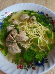 Traditional noodle soup with clear broth, green vegetables, and sliced meatball served in patterned bowl