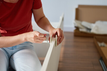 Woman assembling bed frame and fastening details with wrench on wooden floor. DIY home furniture...