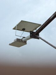 Solar-powered street lamp mounted on tall pole with visible solar panel under overcast sky in urban...