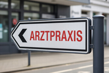 Close up of modern clean direction sign with red text "Arztpraxis" in sunny outdoor setting. Indicates way to medical clinic with blurred background