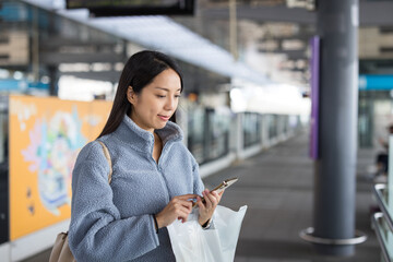 Female commuter standing at subway platform using phone