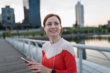 Runner playing music on a smartphone during her morning run across a city bridge.