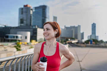 Woman resting after her morning workout, drinking water on a city bridge