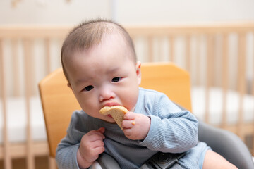 Asian baby sitting on chair eating rice cracker