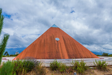 A bold red pyramid stands against a dramatic sky