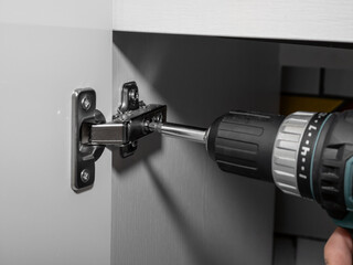 Kitchen hinge screwed to the cabinet, screwdriver close-up, soft-close system