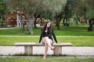 Latin woman, young and beautiful brunette dressed in black and pink heels sitting cross-legged on a...