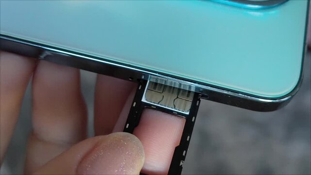 Female hands insert a nano SIM card into the smartphone tray.