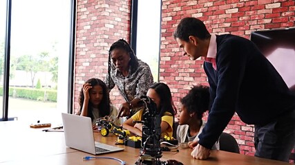 Black female teacher walks with diverse Asian girls in science class working in groups to build robotic arm in elementary school classroom and the girls are happy and enjoying learning works. - Powered by Adobe