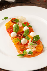Plated tomato and mozzarella arrangement garnished with basil and herbs
