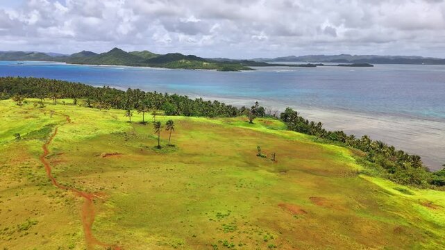 Aerial shot of Corregidor Island, Siargao, Philippines with cogon grass hills, coconut palms, and views of the Pacific Ocean and surrounding bays in a lush tropical coastal landscape.