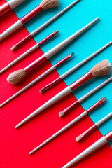 Creative flat lay of a professional makeup brush set displayed symmetrically on a split red and turquoise background. The vibrant color block design emphasizes the contrast and makes the cosmetic