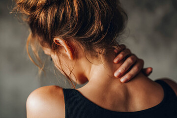 Obraz premium The woman has her hands on her neck, with her back turned, which may indicate pain or tension in that area.
