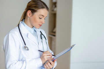 Female doctor writing notes on clipboard with stethoscope in professional environment