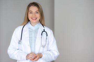 Smiling female doctor in white coat with stethoscope on light background
