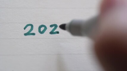 Close up of woman hand writes the number 2026 with a felt tip pen in a notebook. Concept of planning, motivation and setting goals for the coming year. 