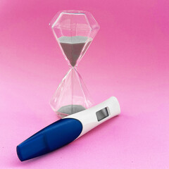 Pregnancy test and hourglass on pink background, symbolizing waiting time and anticipation, healthcare and fertility concept