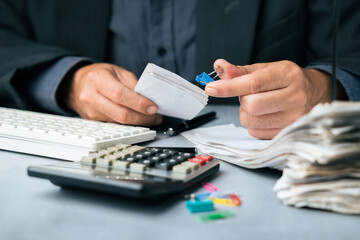 Businessman organizing financial documents with a binder clip at a desk, surrounded by calculator, keyboard, and paper stack, symbolizing accounting and document management tasks