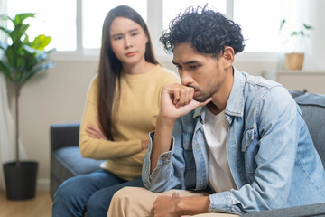 Family problem concept. Tension in relationship between married couple, husband and wife staying sitting separate after quarrel in the living room.