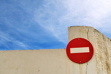 Panneau de sens interdit sur un mur blanc devant le ciel bleu.