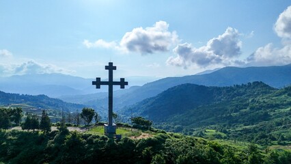 Cross monument on green mountain with scenic valley and blue sky