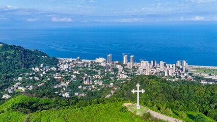 Panoramic city view with sea and cross from green mountain hilltop