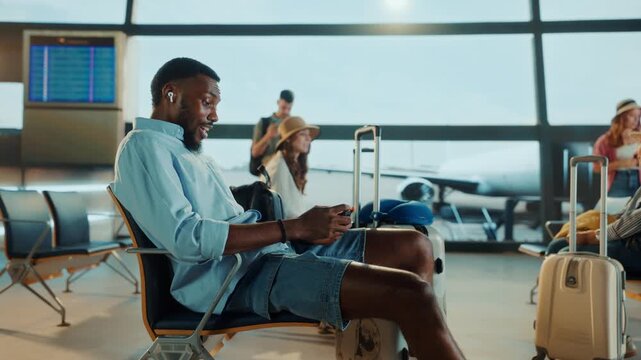 A traveler checks their phone while waiting at the airport gate. Other passengers and a plane are visible in the background.