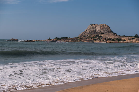 Scenic view of ocean waves rolling onto a sandy beach with a prominent rocky islet in the background, typical of the beautiful Sri Lankan coastline - Powered by Adobe