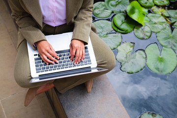 Businesswoman working with laptop by a pond with water lilies outdoors