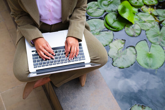 Businesswoman working with laptop by a pond with water lilies outdoors