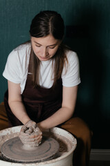 Young woman working with clay at pottery wheel in ceramic studio during creative process