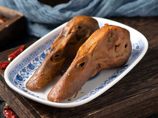 Two braised duck heads on a white plate on a wooden tabletop