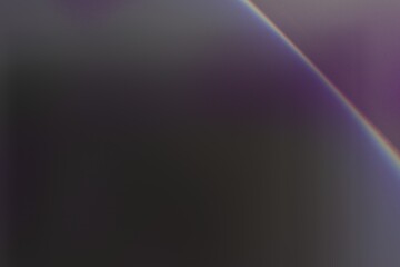 An abstract image featuring a blurred, dark background with a subtle, curved rainbow-like light streak diagonally across it. The colors are muted and blend softly. 