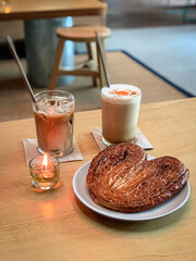 Cozy café setup with a heart-shaped palmier pastry and two iced coffee drinks on a wooden table, perfect for a relaxing coffee break.