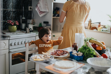 A young child assists in making pizza, surrounded by fresh ingredients on a kitchen table, symbolizing enthusiasm for homemade cooking, family activities, and the joy of meal preparation.