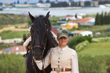 Young and beautiful woman holds with affection the face of her black purebred Spanish horse and...