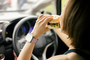 Woman is eating a hamburger while driving to work in the morning