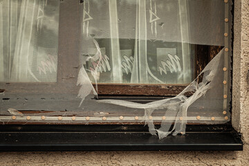 Broken window with torn curtain revealing a glimpse into a forgotten space filled with history and...