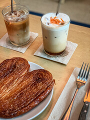 Cozy café setup with a heart-shaped palmier pastry and two iced coffee drinks on a wooden table,...