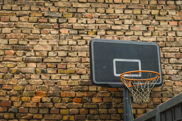 Urban basketball hoop with weathered brick wall background under soft lighting, inviting...