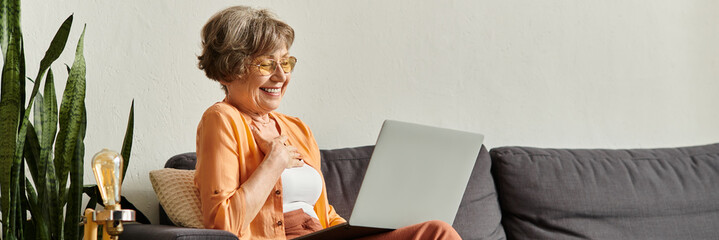Joyful senior woman enjoys cozy moments at home while engaging with technology