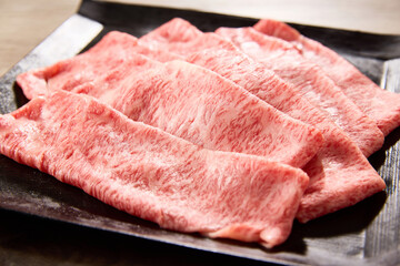 黒毛和牛の霜降りスライス肉を黒い角皿に美しく盛り付けたクローズアップ写真。艶やかな脂と繊細なサシ模様が際立つ高級食材のイメージカット。焼肉やすき焼きに最適。