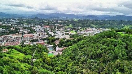Obraz premium This aerial landscape showcases lush green hills with urban development under cloudy skies, captivating the eye