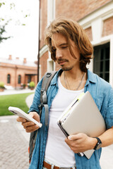 Attractive adult male real estate agent with long hair in stylish denim clothes standing against...
