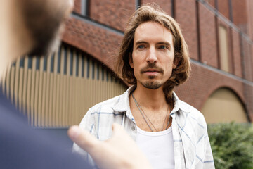 Selective focus on man with long hair listening to his mate gesticulating with hands out of focus...