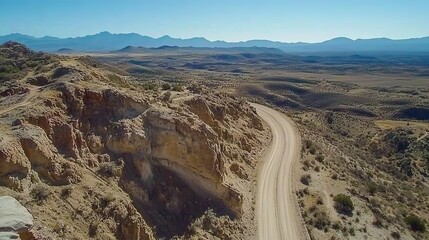 High-angle view of a winding dirt road through a desert landscape.  Rocky cliffs and hillsides frame the road