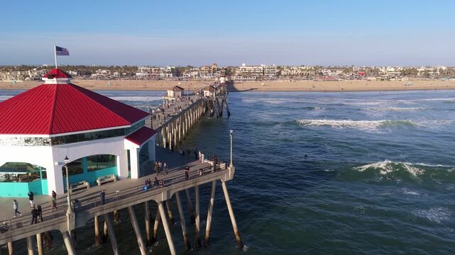 Drone shot of Huntington Beach Pier with a red-roofed building and waves breaking along the coast