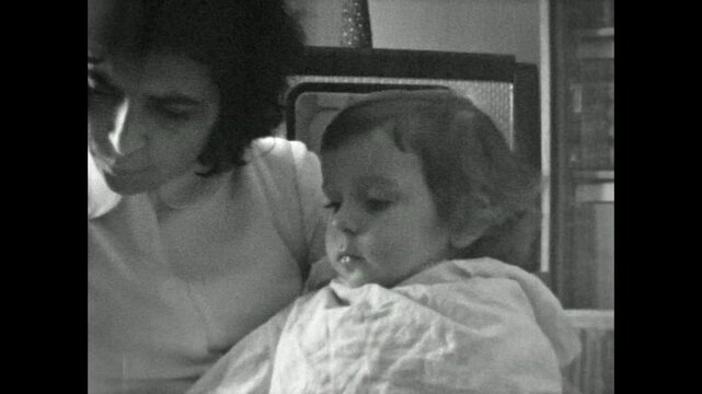 Old archive, caring mother feeding baby with spoon in retro indoor, close up. Cute small child eat home food. Tender motherhood care. Vintage film childhood. Archival retro 1960s. Breakfast nutrition